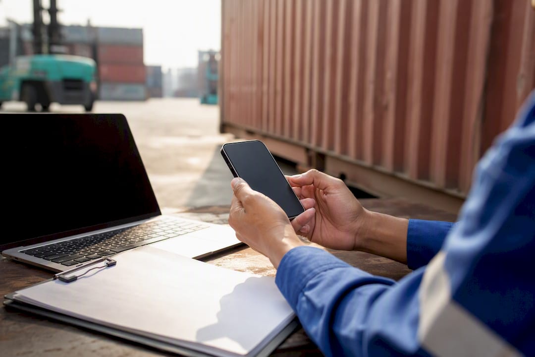 Hands holding phone near shipping model on desk